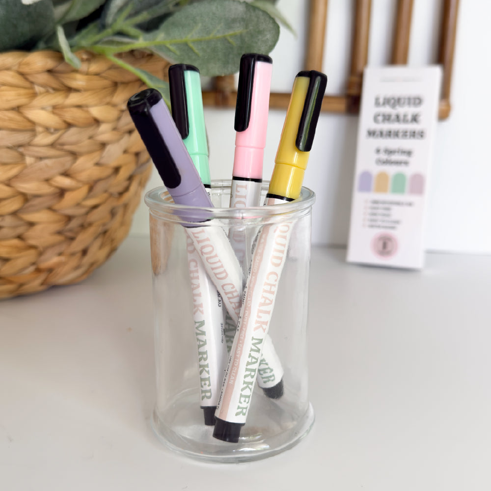 Coloured liquid chalk markers in pastel pink yellow purple and green styled in a glass jar with greenery background